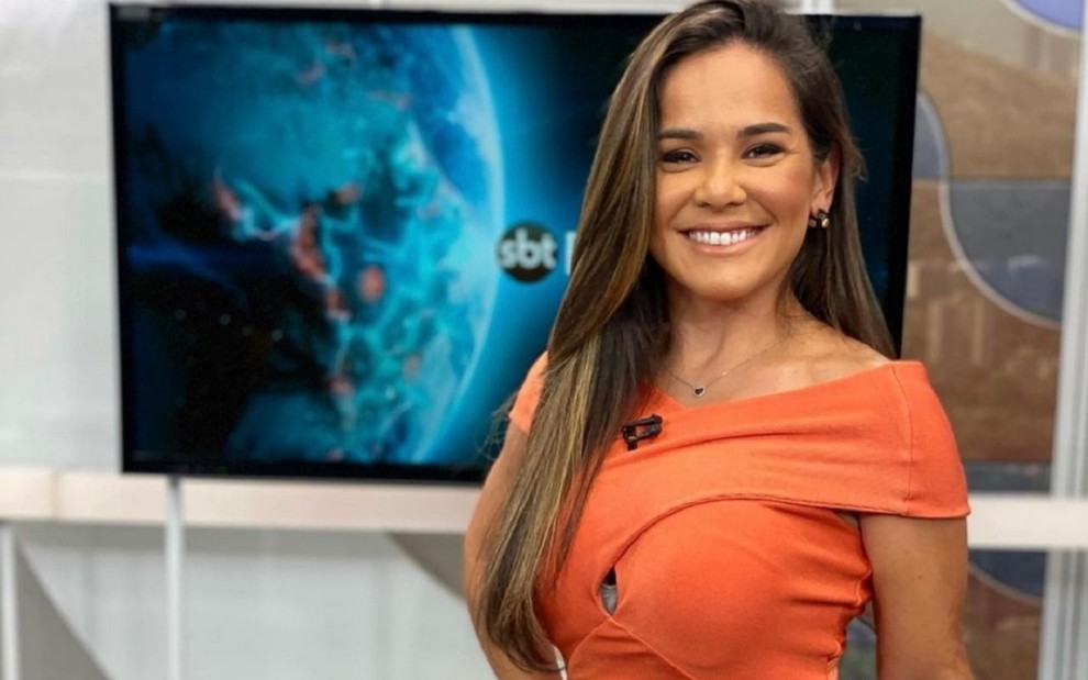 Isabele Benito usa uma roupa laranja e sorri para a câmera no estúdio do SBT no Rio de Janeiro