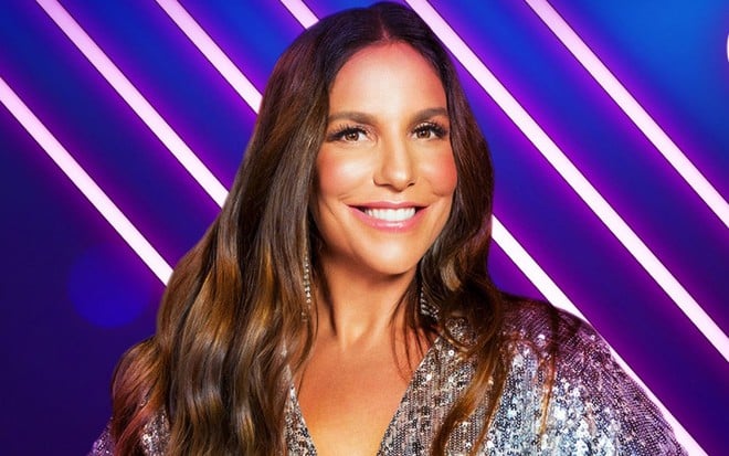 Ivete Sangalo com um vestindo cinza e sorrindo para a câmera. O fundo é azul