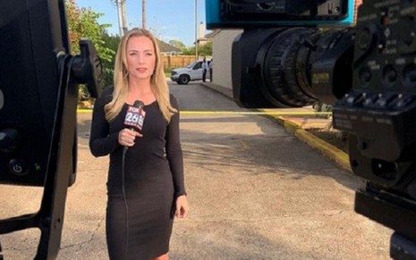 Usando um vestido negro, a repórter Ivory Hecker, segura um microfone da Fox enquanto se prepara para entrar ao vivo no canal de notícias