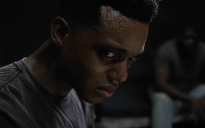 Jabari Banks, interpretando Will, em cena do trailer de Bel-Air. O ator está sentado, com uma camisa cinza, um semblante sério e olhanpo para a câmera de perfil.