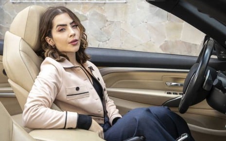 Jade Picon posa dentro de um carro caracterizada como sua personagem em Travessia