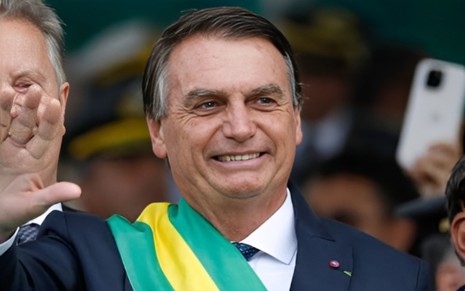 Jair Bolsonaro está no meio da multidão, sorridente, e acena para o público