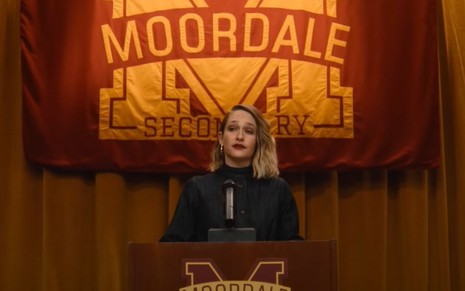Jemima Kirke fala em um palanque com o logo do colégio Moordale ao fundo em cena da nova temporada de Sex Education