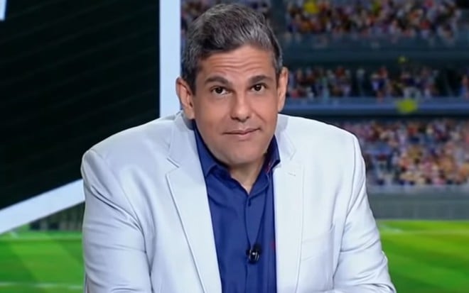 João Guilherme com um blazer branco, calça jeans e camisa azul, no estúdio do ESPN FC