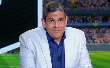 João Guilherme com um blazer branco, calça jeans e camisa azul, no estúdio do ESPN FC