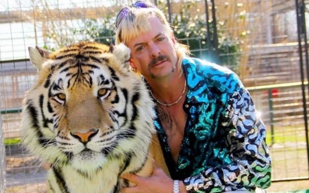 Joe Exotic, de A Máfia dos Tigres, posa em seu zoológico com camisa brilhante e abraçado a um tigre