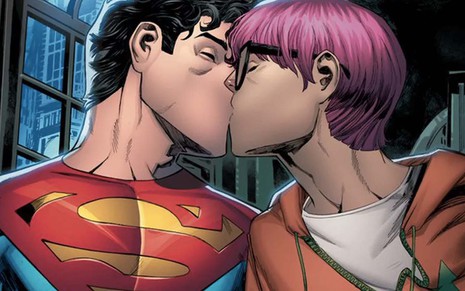 Do lado esquerdo, o Superman em seu uniforme clássico beija outro homem, com cabelos rosa, óculos de aro preto e um moletom laranja