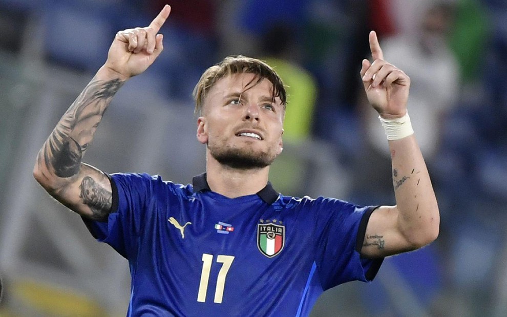 Ciro Immobile com camisa azul da Itália olhando para cima com as duas mãos para o alto na altura da cabeça e com os indicadores levantados em celebração de gol em partida