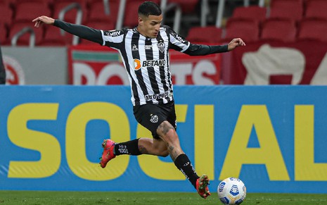 Guilherme Arana com meião e calção preto e camisa preta e branca do Atlético-MG em movimento para chutar a bola com o pé esquerdo em partida