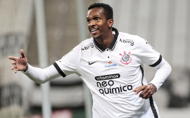 Jô com a camisa branca do Corinthians com camiseta de manga longa por baixo com braços levantados na altura da cinteura olhando para esquerda em partida