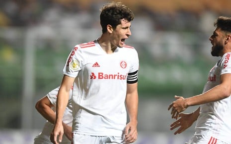 Rodrigo Dourado com o uniforme branco do Internacional com boca aberta e olhando para outro jogador no lado direito em jogo pelo Internacional