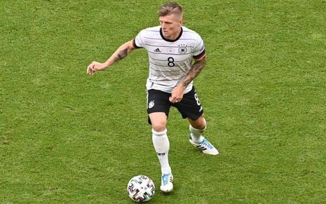 Toni Kroos com a camisa branca com linhas pretas da Alemanha correndo com a bola dominada no pé direito em partida na Eurocopa