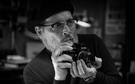 Johnny Depp com uma câmera fotográfica na mão em cena do filme Minamata