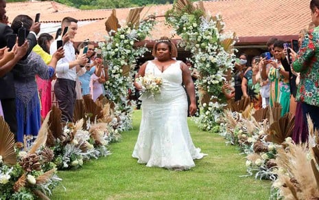 A cantora Jojo Todynha, vista de noiva, com um buquê de flores brancas, entra para se casar em cerimônia ao ar livre
