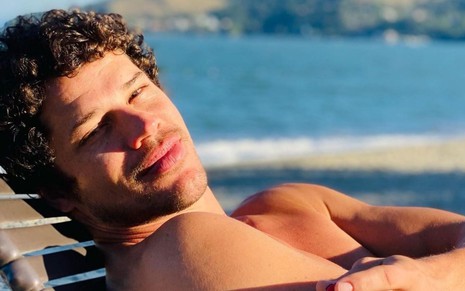 Sem camisa, José Loreto em espreguiçadeira na praia em dia de sol intenso