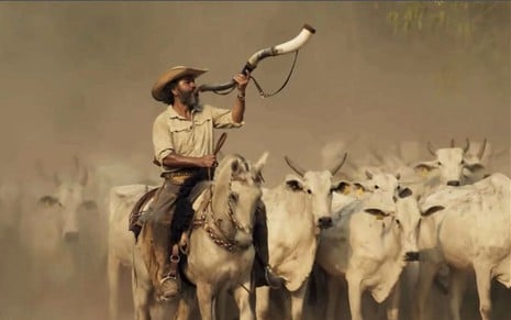 O ator Marcos Palmeira como José Leôncio em Pantanal; ele está em cima de um cavalo tocando o berrante junto à boiada