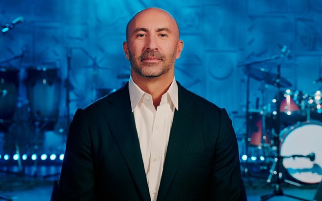 Juan Acosta com um terno preto, camisa branca e sorriso em uma foto na Paramount