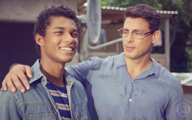 Ravi (Juan Paiva) sorri e olha para o horizonte; Christian (Cauã Reymond) observa o amigo em cena do primeiro capítulo de Um Lugar ao Sol