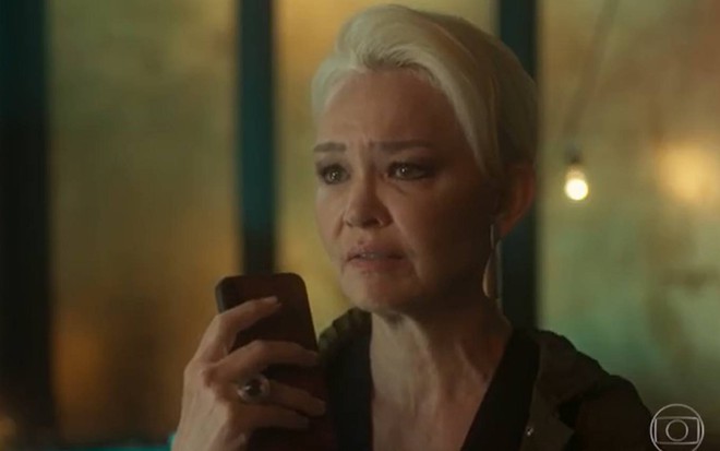 Atriz Julia Lemmertz segura celular e olha para frente com cara de choro em cena de Quanto Mas Vida, Melhor