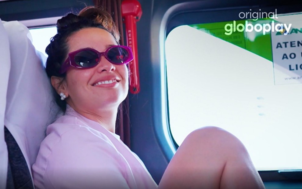 Sorridente e de óculos escuros, Juliette olha para a câmera durante viagem em ônibus