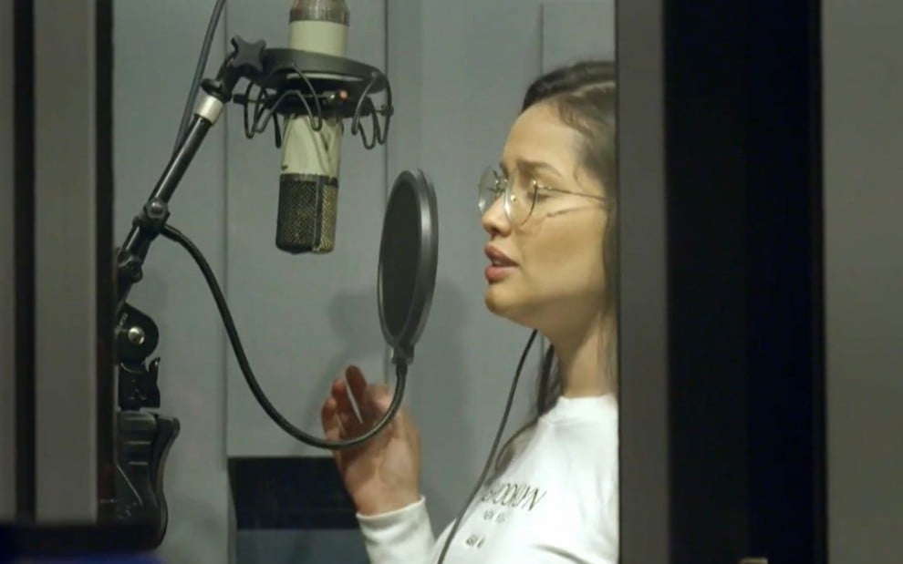 Juliette Freire usa óculos, está de olhos fechados e aparece cantando em um estúdio de gravação