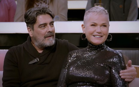 Junno Andrade e Xuxa Meneghel sentados no sofá do programa Sobre Nós Dois