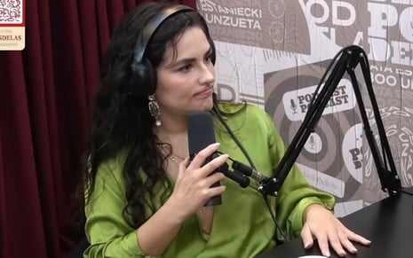 Kéfera no estúdio do Poddelas; ela está sentada, veste uma camisa verde, está de fones de ouvido e um microfona na mão