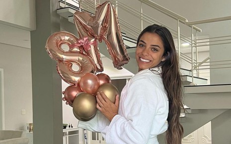 Key Alves está de roupão e segura balões decorativos