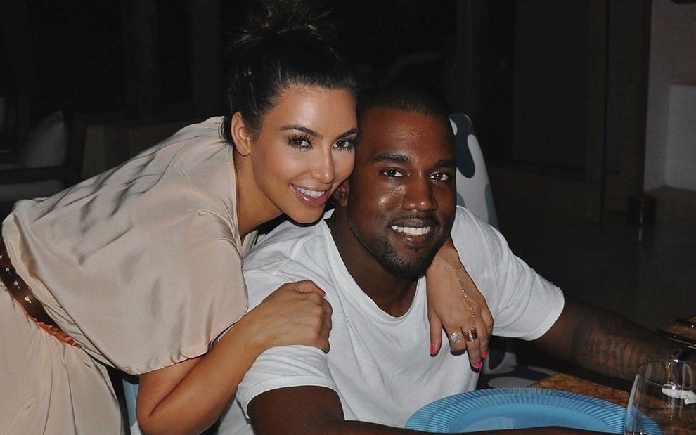 Kim Kardashian de vestido bege abraçada a Kanye West, de camiseta branca
