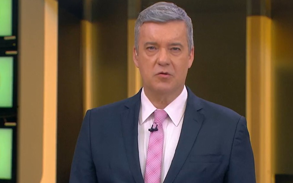 Roberto Kovalick com um terno azul, uma camisa branca e uma gravata rosa nos estúdios do Hora 1 da Notícia, da Globo