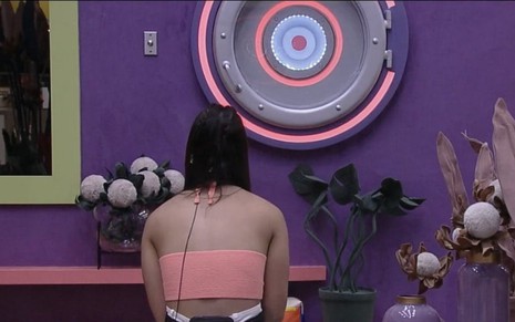 Larissa Tomásia está sentada de costas, e encara atentamente botão de desistência na sala do Big Brother Brasil 22