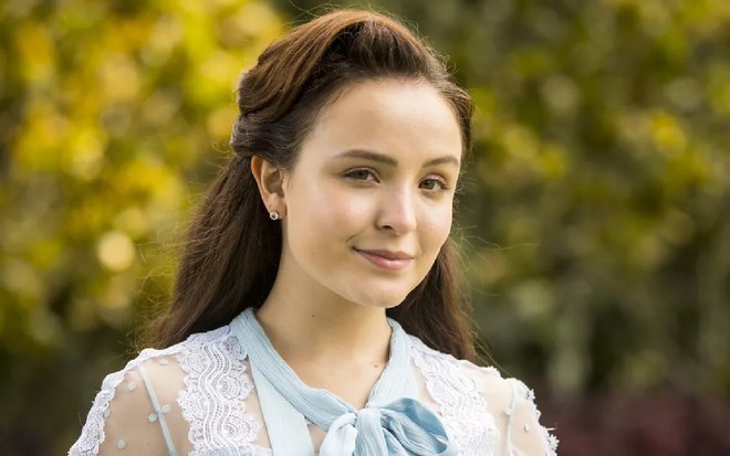 Larissa Manoela com um vestido azul e um leve sorriso nas gravações de Além da Ilusão