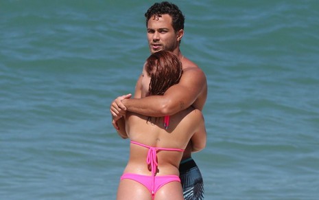 Imagem de Larissa Manoela, de costas e biquíni rosa, e André Luiz Frambach abraçados na praia