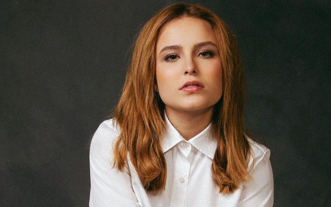 Larissa Manoela posa para a foto, com expressão séria, usando uma blusa branca