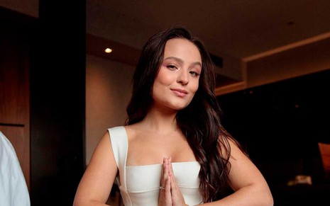 A atriz Larissa Manoela de cabelos pretos e junta as palmas das mãos em sina de zen enquanto medita