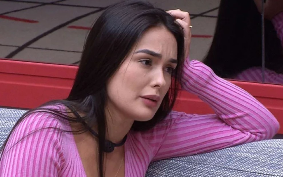 Larissa Santos está com expressão séria no sofá da sala do BBB 23