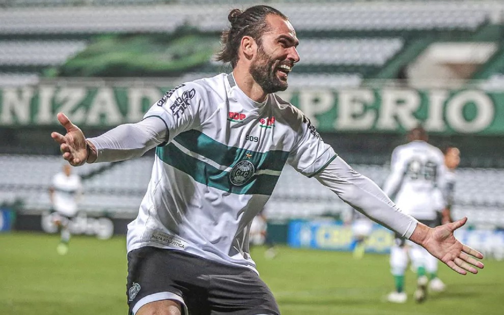 Léo Gamalho comemora gol do Coritiba na Série B. Ele usa uma camisa branca com faixas verdes.