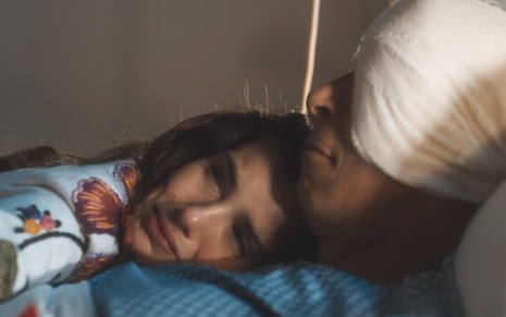 Marê (Camila Queiroz) está deitada no peito de Leonel (Paulo Gorgulho), que está com a cabeça enfaixada, em cena de Amor Perfeito