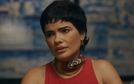 Em cena de Travessia, Vanessa Giácomo está com a expressão de lamento usando camiseta vermelha e lenço no pescoço