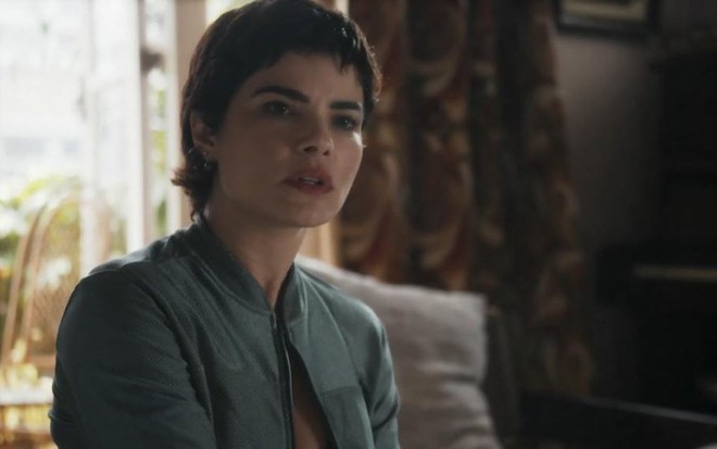 Em cena de Travessia, Vanessa Giácomo está com a expressão de surpresa conversando com alguém; ela usa vaqueta verde
