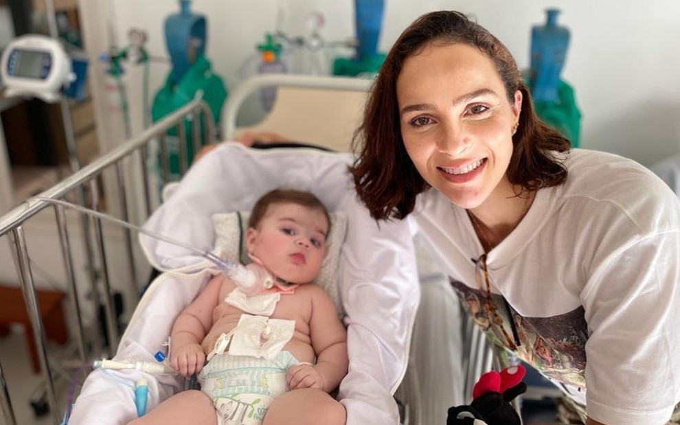 Letícia Cazarré ao lado da filha caçula, Maria Guilhermina, que está num berço, com curativos no corpo