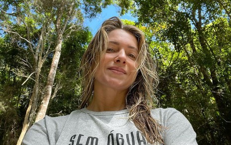 Leticia Spiller de cabelos soltos, veste camiseta cinza em meio à natureza