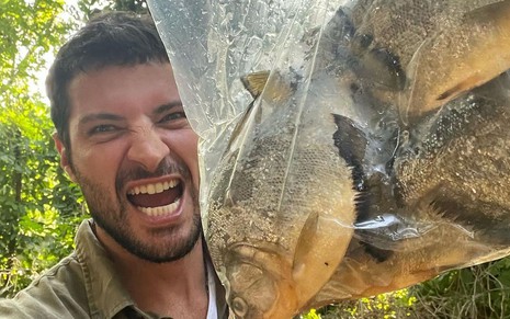 O ator Leandro Lima em foto publicada no seu Instagram; ele está segurando um saco com piranhas e fazendo cara de vingança como quem vai devorar os peixes