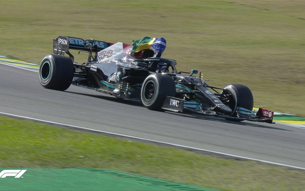 Lewis Hamilton comemora vitória na Fórmula 1, dentro da sua Mercedes, com a bandeira do Brasil na mão
