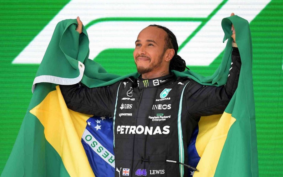 Lewis Hamilton comemora vitória na Fórmula 1 segurando uma bandeira do Brasil