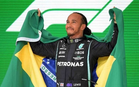 Lewis Hamilton comemora vitória na Fórmula 1 segurando uma bandeira do Brasil