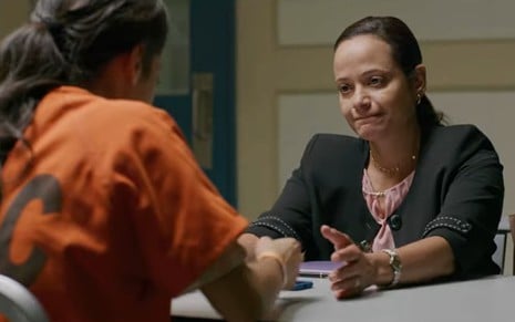 Fátima Molina, de costas e com macacão laranja de presidiária, segura as mãos de Judy Reyes em cena do filme Arrancada dos Braços Dela