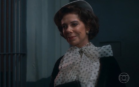 Angela Vieira grava cena como Lisiê em Além da Ilusão; ela está com roupa de época com laço no pescoço e chapéu