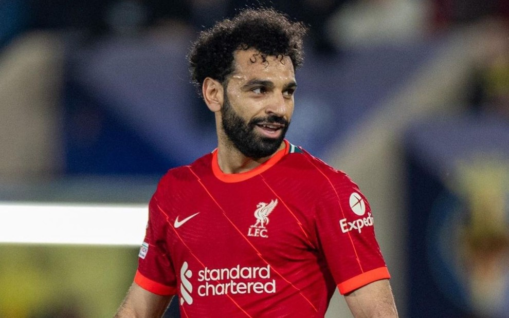 Salah, do Liverpool, caminha em campo e veste uniforme vermelho com detalhes branco e laranja