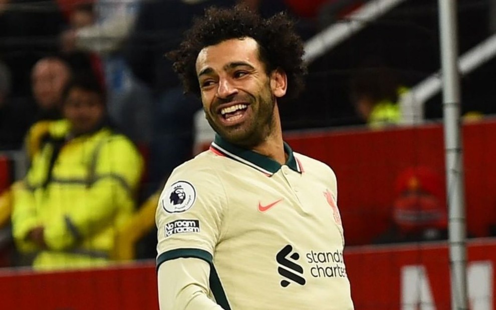Mohamed Salah, do Liverpool, vestindo uniforme bege com detalhes verde, sorrindo e comemorando gol
